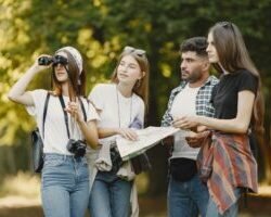 A diverse group of friends use a map and binoculars in a park, enjoying a sunny day outdoors.