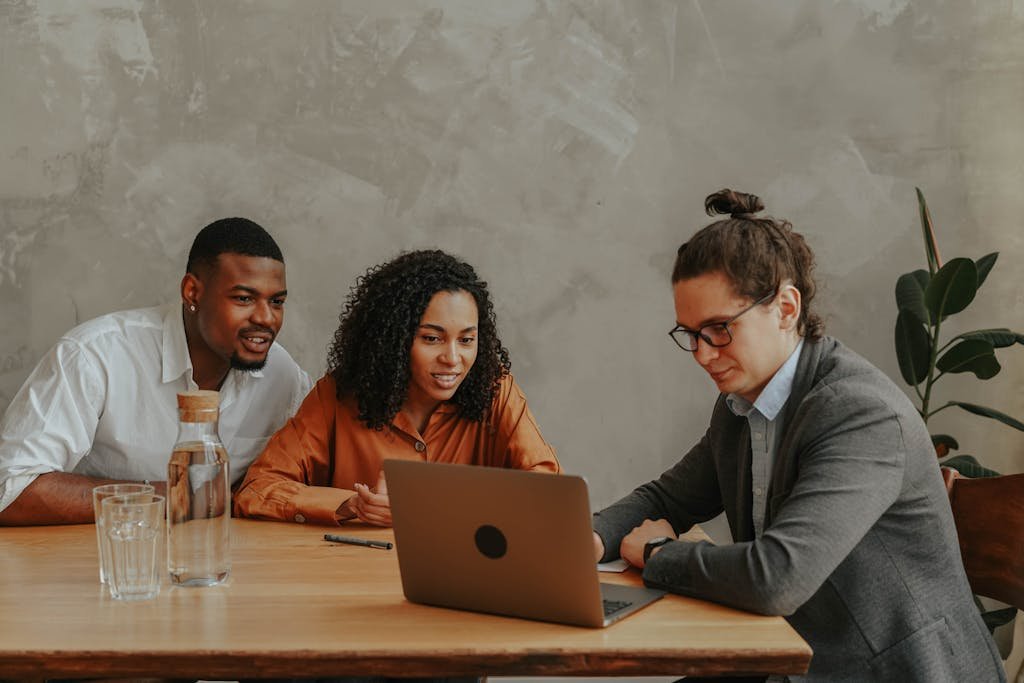 Three coworkers engaged in a collaborative meeting using a laptop, indoors at an office setting.
