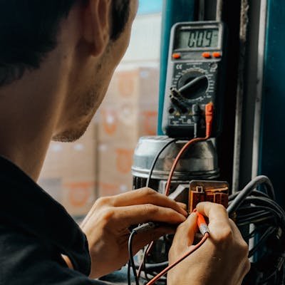 Electrician using a multimeter to check voltages in an industrial setting.