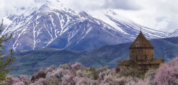 Picturesque landscape of Akdamar Church amidst blooming trees and snow-capped mountains in Van, Turkey.