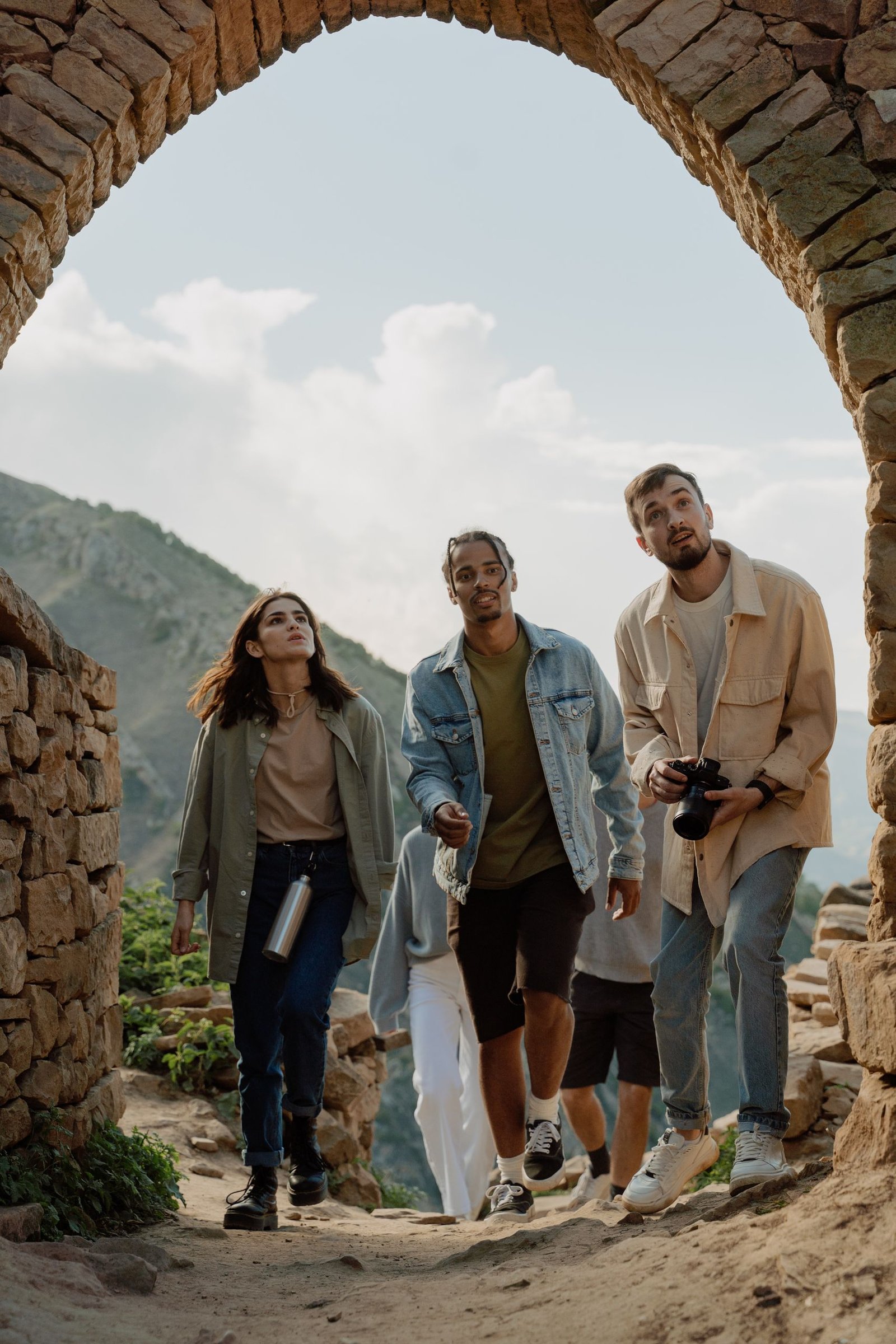 A group of young tourists exploring ancient stone ruins under a brick archway.