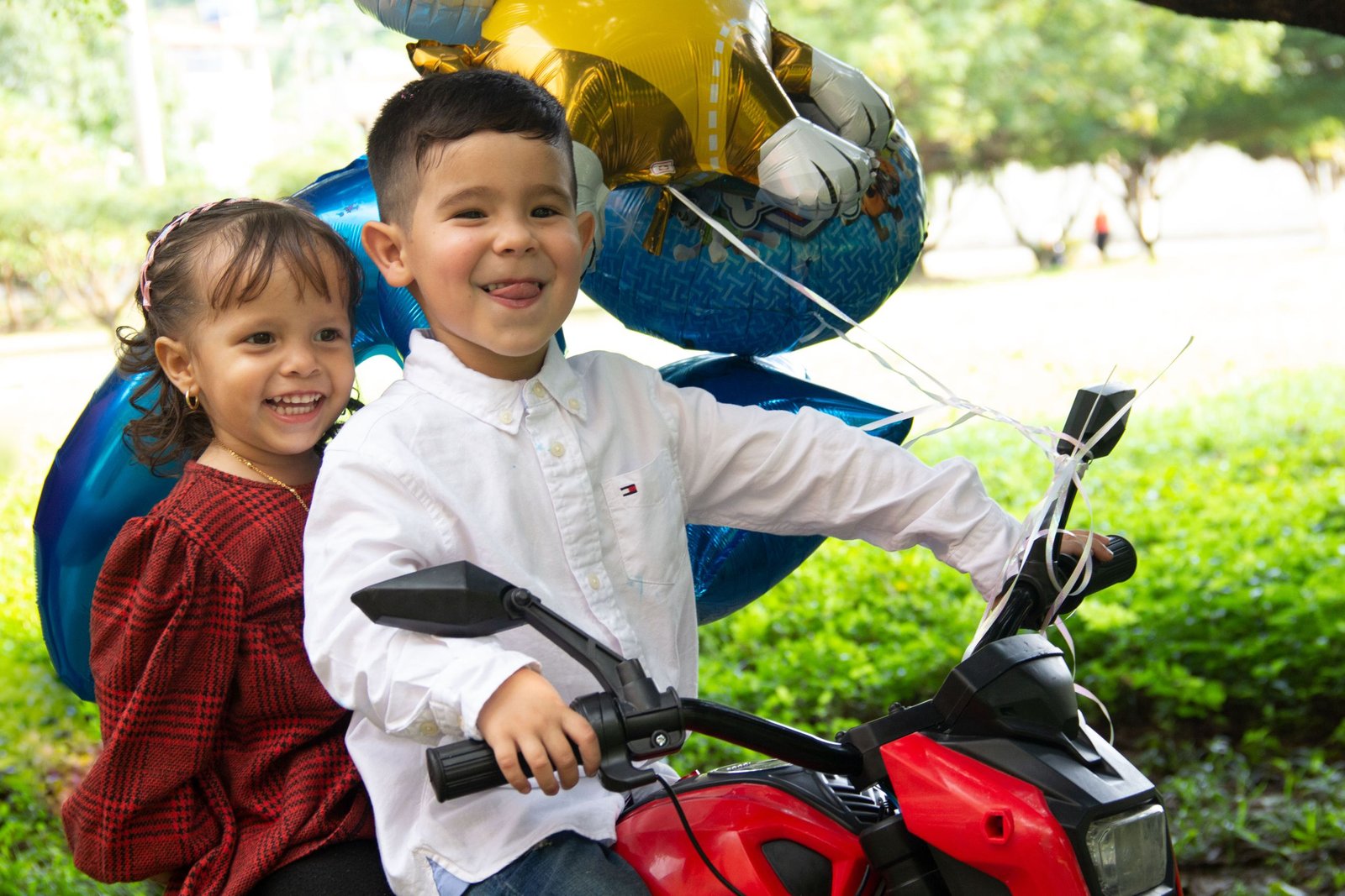 Cheerful children enjoying an outdoor birthday celebration with balloons and a toy quad bike.