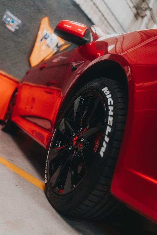 Close-up of a sleek red sports car showcasing a Michelin tire in a garage setting.