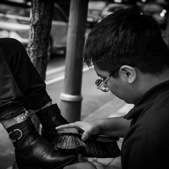 Man polishing shoes on a busy street in Ciudad de México, capturing urban life.